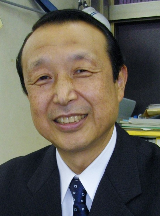 Smiling Asian man in a dark suit and tie in an office setting facing the camera